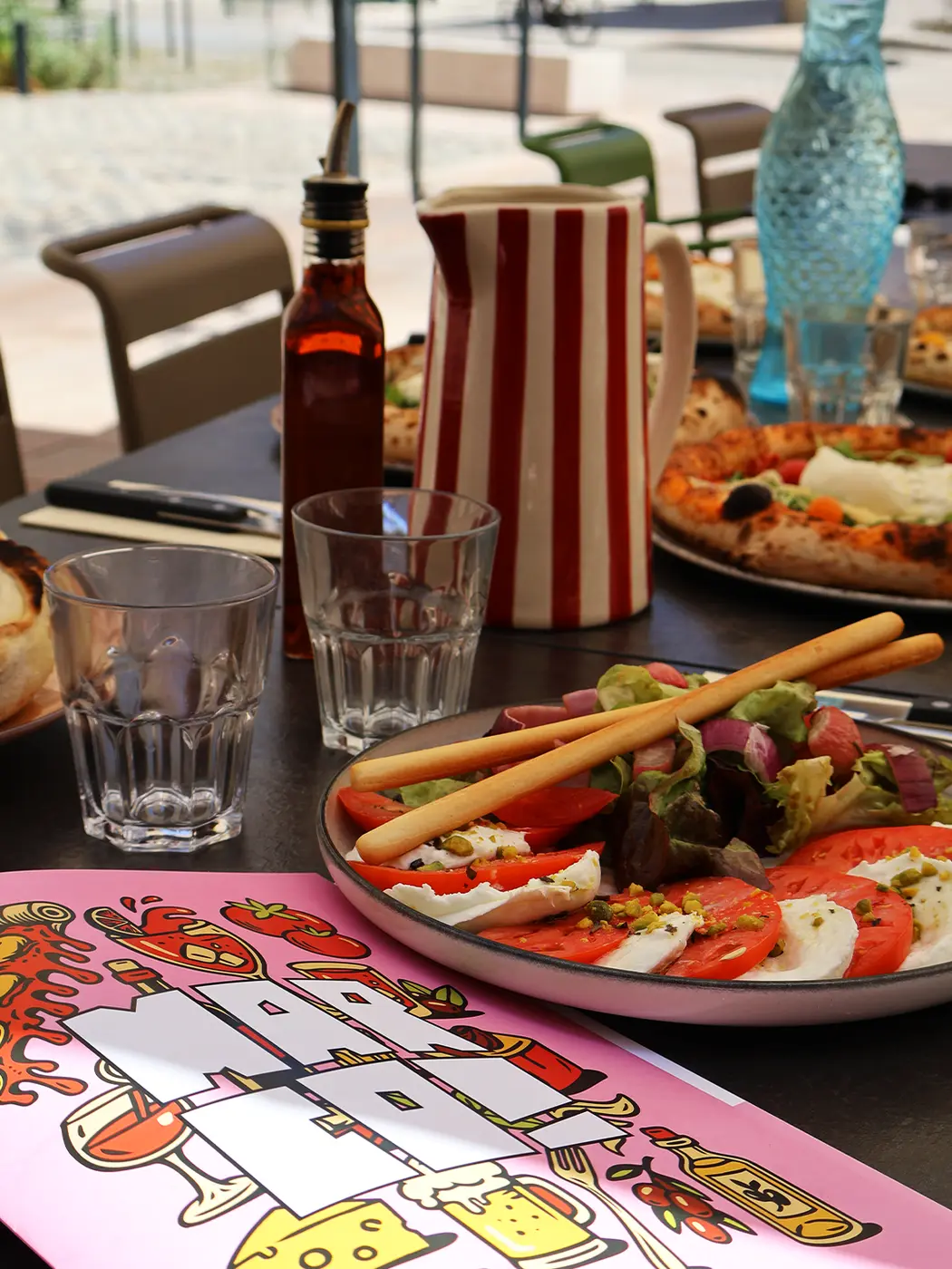 Table dressée avec le menu illustré, tomates mozzarella et pizzas